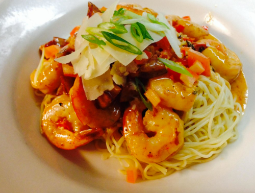 A plate of shrimp pasta topped with vegetables and garnished with green onions and cheese.