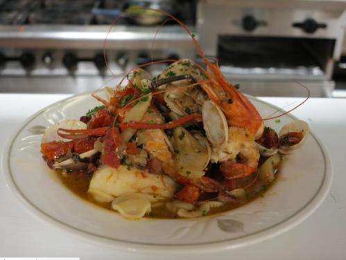 A plate of seafood featuring shrimp, clams, and tomatoes, garnished with herbs, served in a rich sauce.