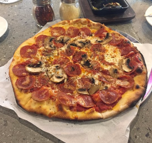 A freshly baked pepperoni pizza topped with mushrooms, cheese, and herbs on a gray countertop.