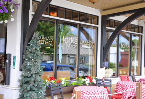 Exterior of a bistro with large windows, a festive tree, and checkered tablecloths on outdoor tables.