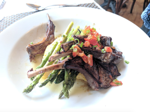 A plate of grilled lamb chops served with asparagus and topped with diced tomatoes and green onions.