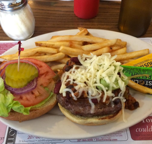 A plate with a burger topped with cheese, lettuce, tomato, onion, and pickles, served with a side of fries.