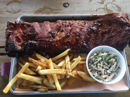 A tray with a large rack of ribs, golden fries, and a small cup of coleslaw on a wooden table.