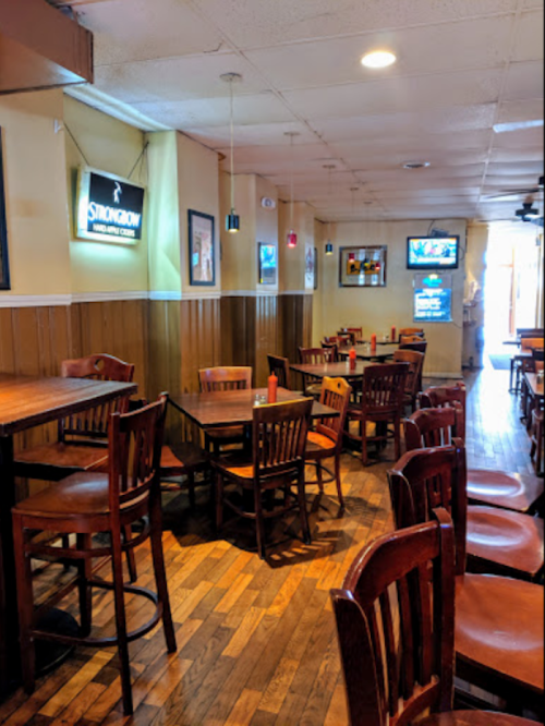 A cozy restaurant interior with wooden tables and chairs, warm lighting, and a few TVs on the walls.