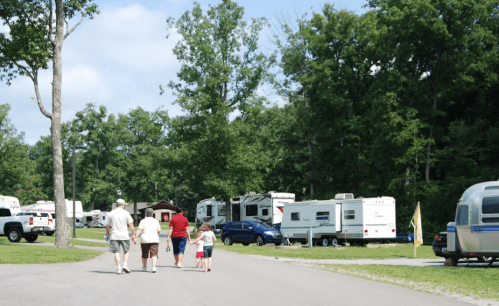 A family walks down a tree-lined road in a campground with RVs parked along the sides.