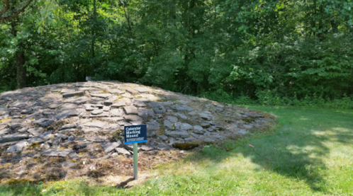 A stone mound surrounded by trees, with a sign reading "Caldender Mound" in a grassy area.