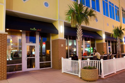 Exterior view of a restaurant with outdoor seating, palm trees, and a welcoming entrance at night.
