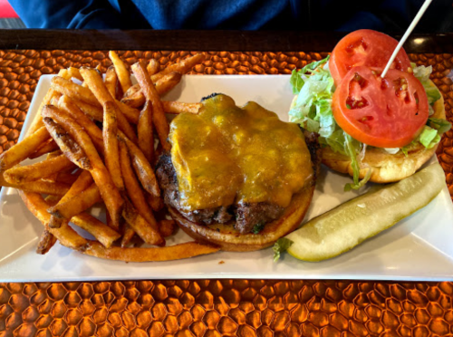 A plate with a cheeseburger topped with melted cheese, lettuce, and tomato, served with crispy fries and a pickle.