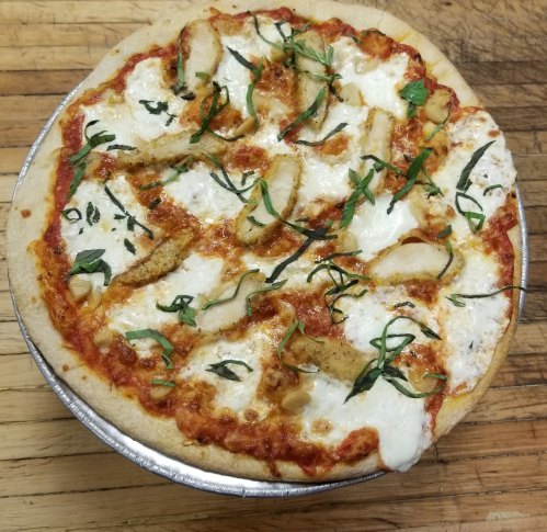 A freshly baked pizza topped with marinara sauce, mozzarella cheese, sliced chicken, and fresh basil on a wooden surface.