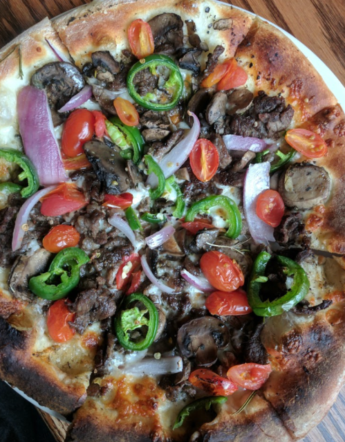 A close-up of a pizza topped with mushrooms, beef, tomatoes, green peppers, and red onions on a golden crust.