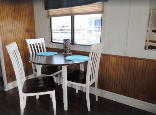 A small dining area with a round table, four white chairs, and blue placemats, near a window with a view.