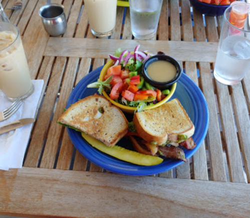 A plate with two sandwiches, a side salad with tomatoes and dressing, and a pickle, on a wooden table.