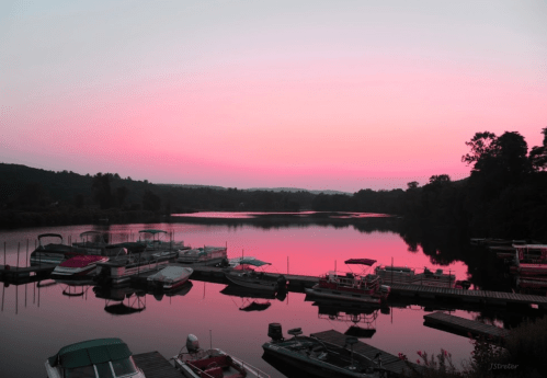 A serene lake at sunset, with boats docked and a pink sky reflecting on the water's surface.