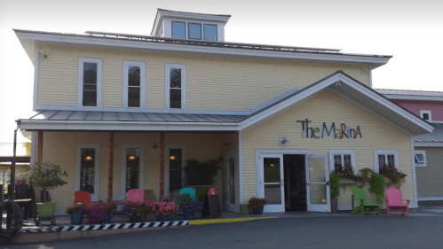 A charming yellow building with a sign reading "The Marina," featuring colorful chairs and flower pots outside.