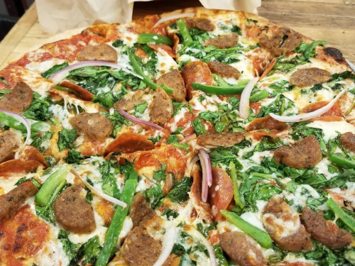 A close-up of a pizza topped with spinach, green peppers, pepperoni, onions, and sausage on a crispy crust.