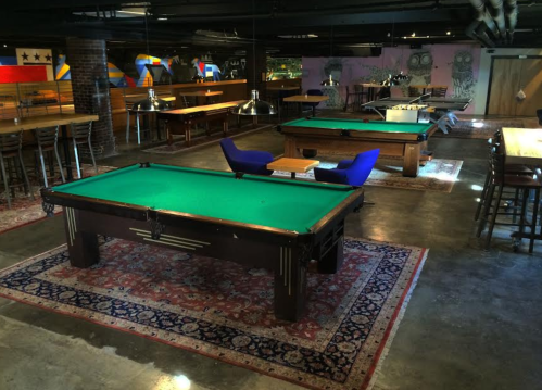 A spacious game room featuring pool tables, seating areas, and colorful wall art.