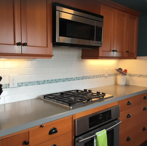 A modern kitchen with wooden cabinets, a microwave, and a gas stove on a gray countertop with a white backsplash.