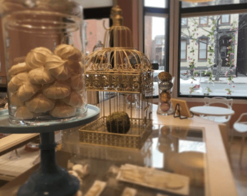 A cozy dessert shop interior featuring meringues in a jar and a decorative birdcage with greenery.