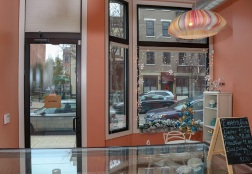 Interior of a cozy café with orange walls, a colorful lamp, and a decorated window displaying a holiday tree.
