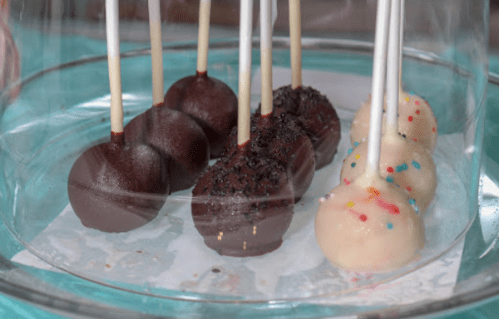 A glass display case with chocolate and vanilla cake pops, some topped with sprinkles and others with a chocolate coating.