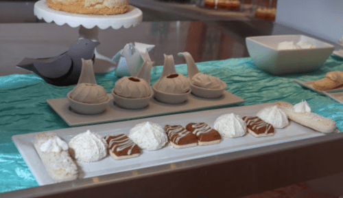A dessert display featuring meringues, cream-filled pastries, and a cake, with decorative bird-shaped elements.
