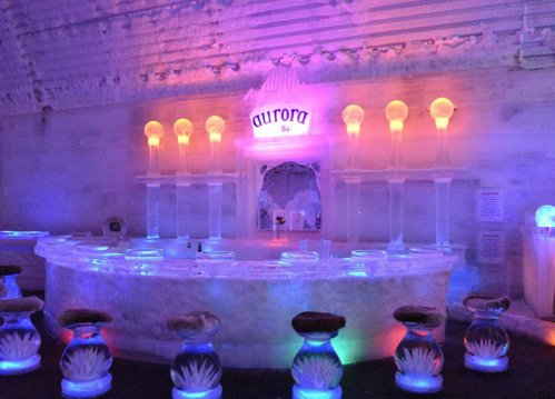 A stunning ice bar with colorful lighting, featuring a curved ice counter and unique ice stools.