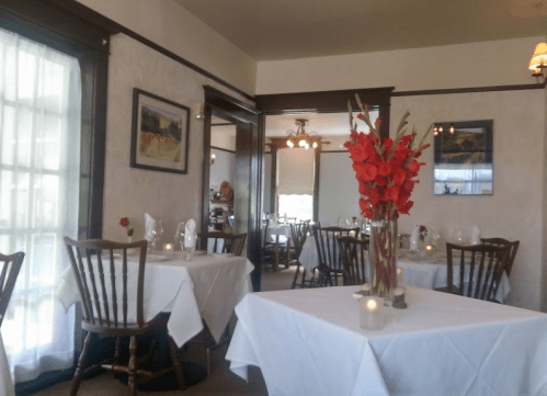 Cozy restaurant interior with white tablecloths, floral centerpieces, and soft lighting.