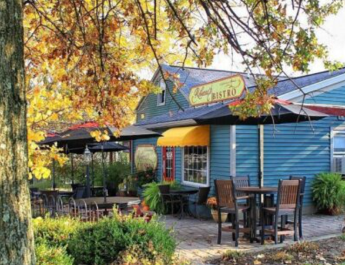 Charming bistro with outdoor seating, surrounded by autumn leaves and greenery. Cozy atmosphere on a sunny day.