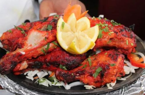 A sizzling platter of tandoori chicken garnished with lemon slices and fresh herbs, served on a bed of onions.