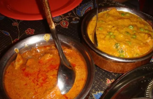 Two bowls of Indian curry dishes, one with a rich red sauce and the other with a creamy orange sauce and green peas.