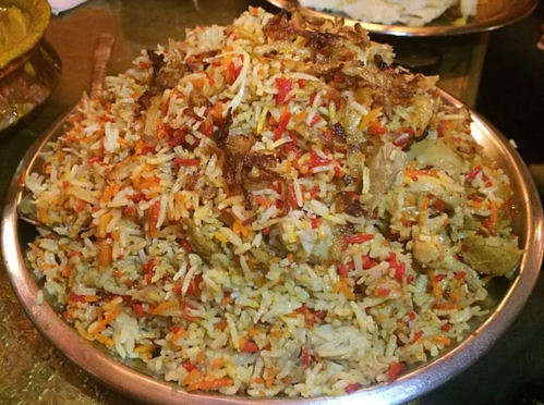 A large serving of colorful biryani with rice, spices, and pieces of meat, presented in a metal dish.