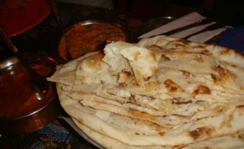 A plate of freshly baked naan bread with a side of curry in metal bowls.