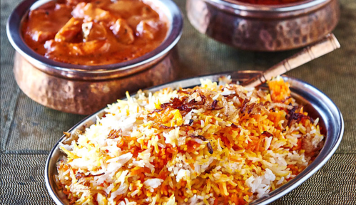 A silver platter of colorful biryani rice garnished with fried onions, alongside two bowls of curry.