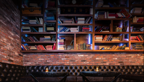 Cozy interior of a library-themed café with a brick wall and shelves filled with books. Two tables in the foreground.