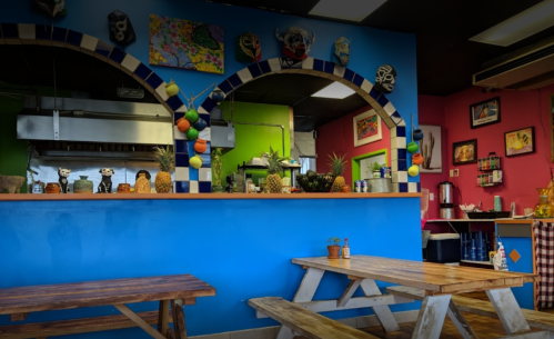 Colorful interior of a restaurant featuring a blue wall, wooden tables, and a vibrant counter with decorative fruits.
