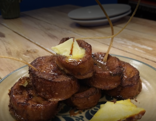 A stack of golden-brown French toast topped with butter and syrup, served on a decorative plate.