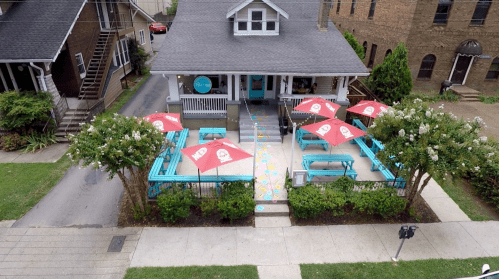 Aerial view of a colorful outdoor dining area with red umbrellas and turquoise seating outside a house.