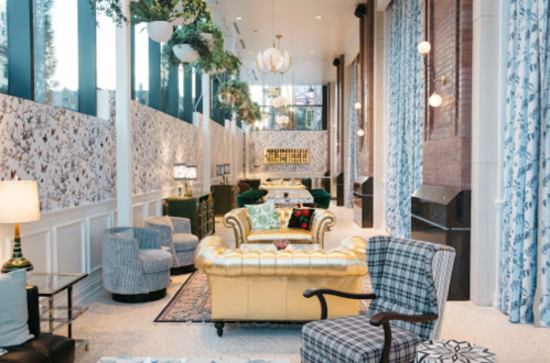 A stylish lounge with a gold sofa, patterned chairs, and large windows, featuring floral wallpaper and elegant decor.