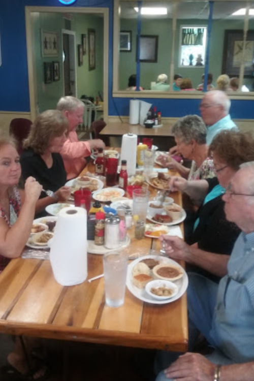 A group of people enjoying a meal together at a restaurant, with plates of food and drinks on the table.