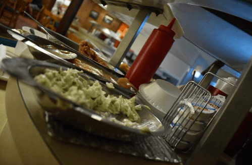 A buffet table with various dishes, including fried chicken, salad, and condiments in a dining area.