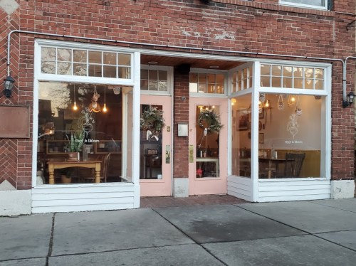 Exterior of a cozy restaurant with large windows, pink door, and festive wreaths, set in a brick building.