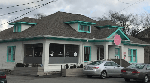 A charming white building with a gray roof and turquoise accents, featuring large windows and a welcoming entrance.