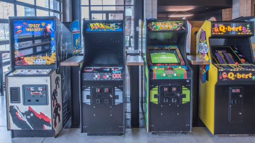 A row of vintage arcade game machines, including Space Invaders, Jungle King, and Q*bert, in a modern setting.