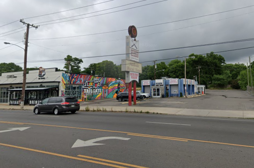 A street view of a colorful mural on a building, with nearby shops and cloudy skies overhead.