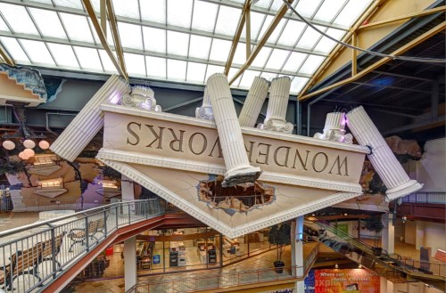 Upside-down building facade with large columns and the word "Wondersworks" in a shopping center.