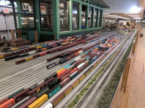 A detailed model train layout featuring numerous colorful freight cars on tracks, set in a spacious indoor environment.