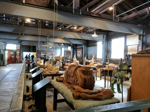 A spacious workshop filled with wooden sculptures, tools, and workstations, showcasing a creative woodworking environment.