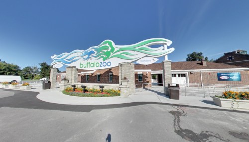 Entrance to Buffalo Zoo featuring a colorful sign and landscaped area with flowers. Clear blue sky above.