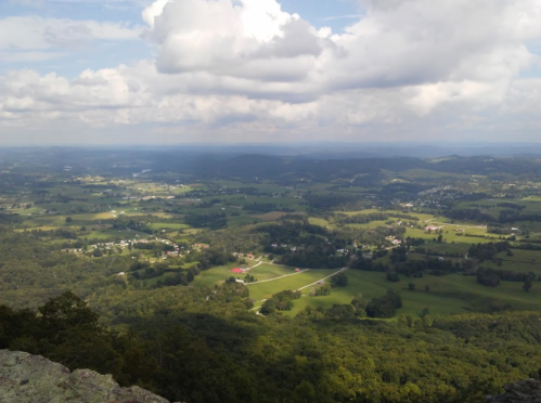 A panoramic view of rolling green hills and valleys under a partly cloudy sky.
