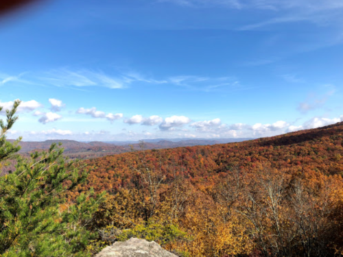 A scenic view of a colorful autumn landscape with rolling hills and a blue sky dotted with clouds.